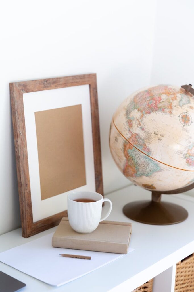 Vintage globe near blank frame and cup of tea placed on book in office